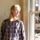 Man with shoulder-length blonde hair look stands next to a window looking outside. Image is connected to a story about autism diagnosis in adulthood.