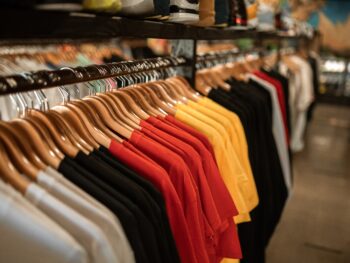 A row of t-shirts hanging on from a rack in a store. The t-shirt colors are white, black, red, and yellow.