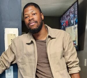 Picture of artist Jon-Keith Gary wearing a light tan jacket and a light brown shirt.