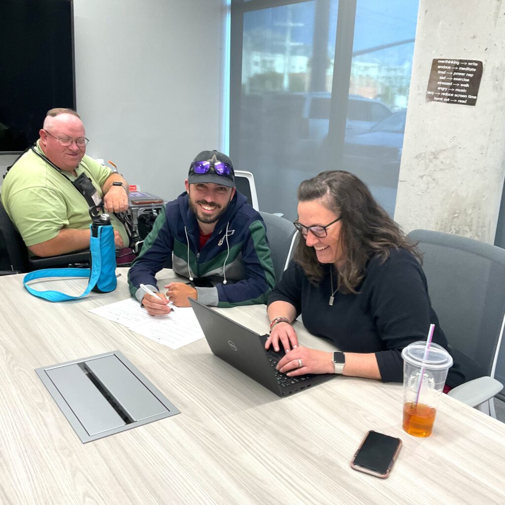 Three people are smiling in a meeting around a conference table