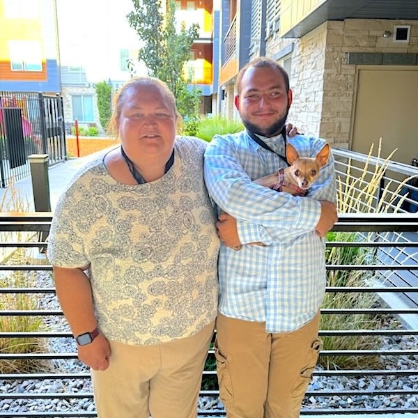 Rebecca has arm around her adult autistic son Austin as they smile standing on an outdoor patio