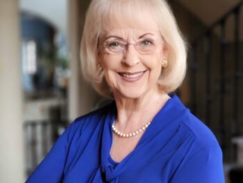 Older woman with chin-length hair and blue blouse smiles at the camera.