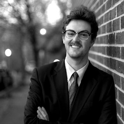 ChadHoopes Person standing with arms folded, leaning against brick wall, smiling.